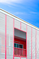 Modern house in minimal style with white wooden battens and pink balustrade on terrace against blue sky background in vertical frame