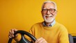© Aliaksandr Siamko - Smiling elderly man holding a steering wheel against a yellow background representing senior activity