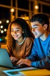 © Tanya - Diverse college students, an African girl and an Caucasian boy in blue brown sweatshirts, focus on a laptop, embodying teamwork and academic engagement.