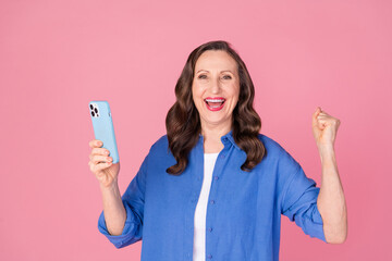 Poster - Photo portrait of nice pensioner female hold device winning wear trendy blue outfit isolated on pink color background