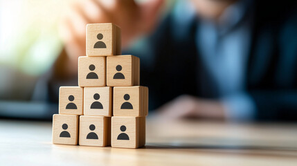 Wooden blocks with minimalist person icons stacked in a pyramid formation on a pale surface, evoking a sense of leadership, organization, and social hierarchy within human resource