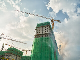 Construction site with cranes and green netting under a cloudy sky