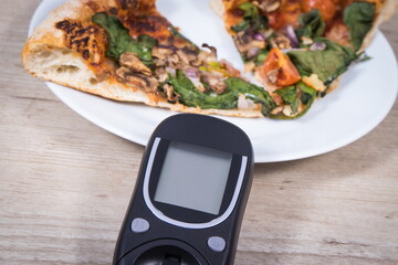 Glucometer for checking sugar level and fresh baked vegetarian pizza. Nutrition during diabetes