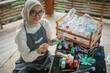 © Odua Images - hijab woman posing at camera while painting recycled plastic bottle waste