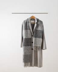 soft grey casual wool coat with long fluffy alpaca scarf hanging on metallic hanger against white wa