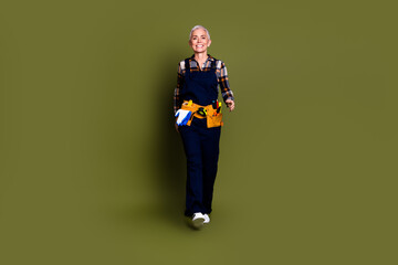 Poster - Full size photo of pretty senior female professional expert handyman walking wear blue workwear overall isolated on khaki color background