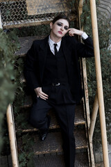 Portrait of stylish and attractive Caucasian young brunette woman in a suit, posing on the street sitting on iron stairs. Beauty, fashion, style. Well-dressed model.