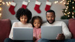 © ChanaphaStudio - A family enjoys time together during the holidays, using laptops, with festive decorations and stockings in the background.