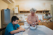 © qunica.com - A grandmother prepares a fresh salad in a warm kitchen while her grandson watches attentively. The scene captures family bonding, tradition, and homemade cooking.