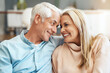 © CamPen2000/peopleimages.com - Love, mature couple and smile on couch in home with romance, relax and affection in marriage. Happy people, embrace and laughing on sofa in lounge for support, security and commitment in relationship