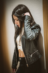 Young woman leaning against the wall while holding her hair, looking down.