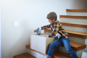 Packing, moving and kid with tape for boxes on stairs for new start, real estate or property investment. Change, male child and boy with cardboard for relocation, helping or seal on package in home