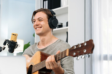 Host channel in smart singer with smiling face, playing guitar along singing, broadcasting on social media channel, wearing headphones to record video streamer at modern studio recording. Pecuniary.