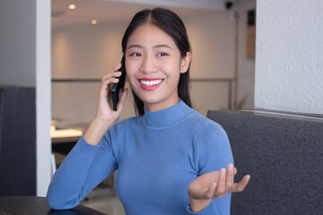 Close-up photo of a young Asian girl, holding a mobile phone and smiling business talking 