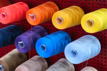 Poster - A row of colorful spools of thread hanging on a red wall. The spools are of different colors and sizes, and they are arranged in a neat and orderly fashion
