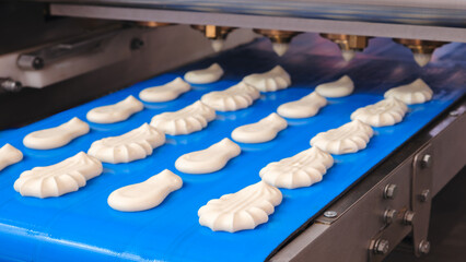 Poster - A conveyor belt is filled with a variety of pastries, including cookies and cakes. The pastries are being made in a factory setting, and the conveyor belt is blue in color