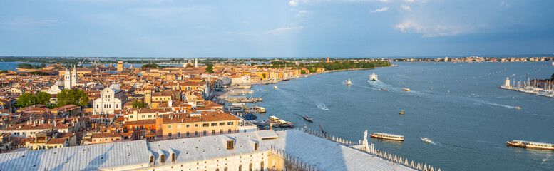 An expansive aerial view captures the iconic canals and historic buildings of Venice as the sun sets, illuminating the city with a warm glow and creating a picturesque atmosphere.