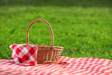 Poster - One picnic wicker basket with checkered napkin and blanket on green grass. Space for text