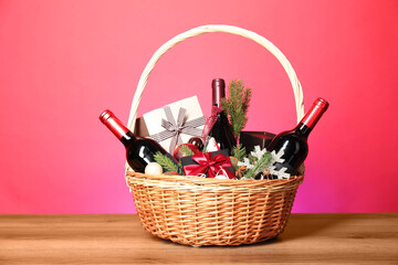 Canvas Print - Wicker gift basket with wine on wooden table against pink background