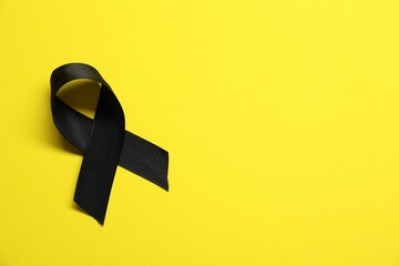 Wall Mural - Black awareness ribbon on yellow background, top view. Space for text