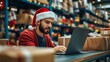© Valentyna Prudnikova - Festive warehouse worker in Santa hat diligently working on laptop amid stacked packages and twinkling lights, embodying holiday season hustle and cheer.