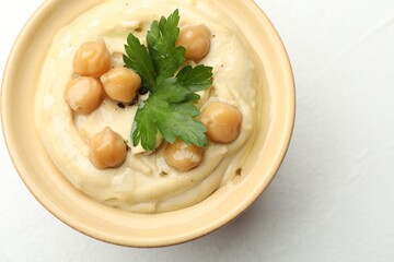 Delicious hummus with parsley and chickpeas in bowl on white table, top view