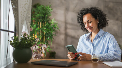 mature woman sit and use mobile phone while drink coffee at home