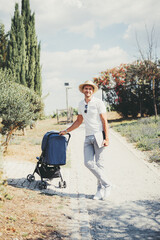 a smiling man in casual summer attire with a straw hat, white shirt, and gray pants stands on a sunn