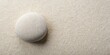© Theerawat - A single smooth, white stone rests on a bed of fine, grainy sand, creating a minimalist and serene visual