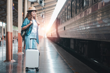 A young woman traveler with a suitcase stands on a train platform at sunset, ready for her journey in a modern train station.