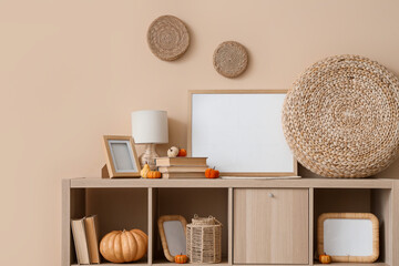 Photo frames, books and pumpkins on shelf unit near beige wall in room