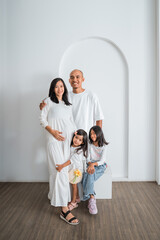 A beautifully pregnant woman is smiling and posing for a memorable picture alongside her loving husband and their two adorable daughters