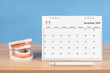 © gamjai - November monthly desk calendar for 2024 year and model dentures on the table.