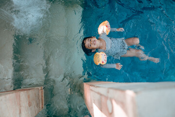 A young child delightfully enjoys floating in a refreshing pool, wearing colorful arm floats