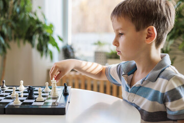 Children brothers play chess at home at a round white table in the living room on a chessboard. 