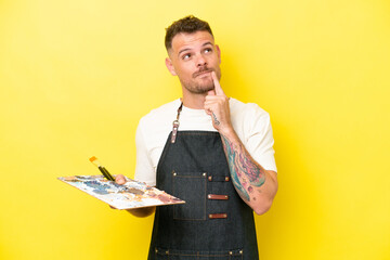 Wall Mural - Young artist caucasian man holding a palette isolated on yellow background having doubts while looking up