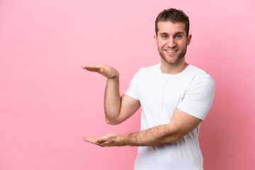 Wall Mural - Young caucasian man isolated on pink background holding copyspace to insert an ad