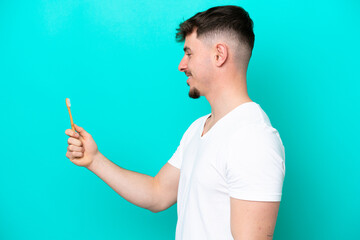 Young caucasian man brushing teeth isolated on blue background with happy expression