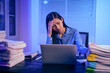© NanSan - An Asian woman works late at night in the office, busy and stressed while checking documents at her desk. She looks tired, managing a heavy workload and feeling the pressure of deadlines