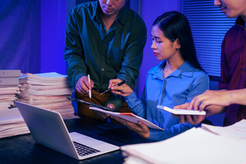 Three young businessmen work together in the office at night, busy on their laptops, checking documents, and finding solutions for an important meeting tomorrow.They are focused and working overtime