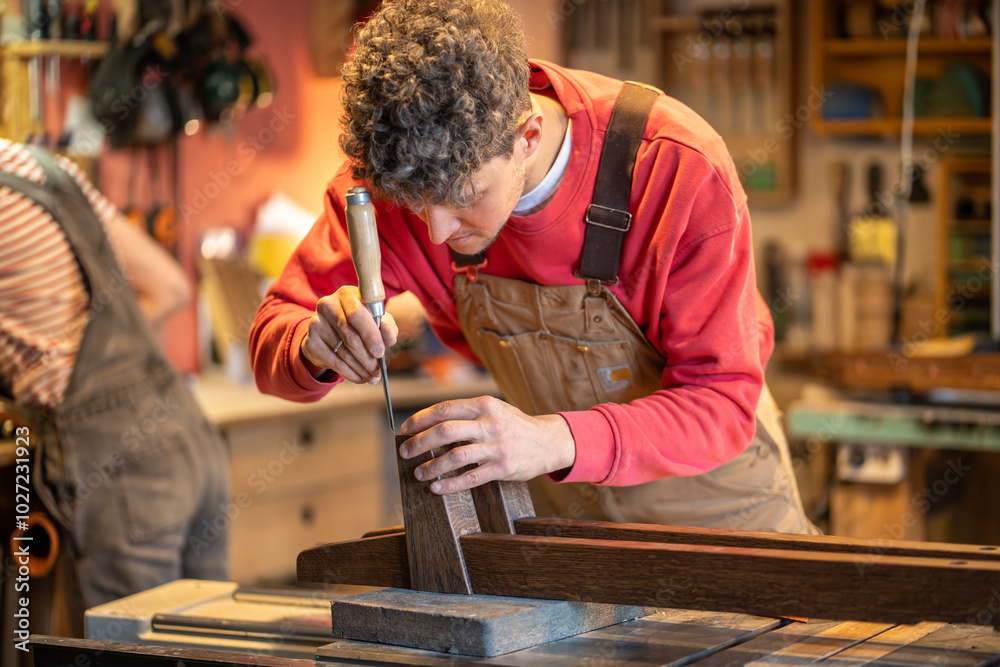 Focused carpenter immersed in work use chisel to smooth bed legs in ...