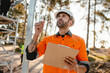 © Austockphoto - A bearded man looking up holding a pen and clipboard on construction site