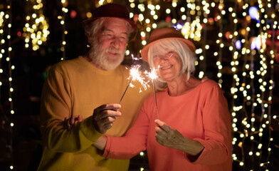 Blurred caucasian senior couple holding sparklers celebrating new year. Happy lifestyle for mature retirees, party lights