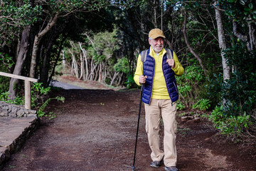 Smiling senior man with walking stick enjoying nature outdoors in a mountain forest walking in the footpath.  Elderly caucasian man enjoys retirement and healthy lifestyle