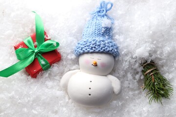 Sticker - Cute decorative snowman, fir tree branches and gift box on artificial snow, flat lay