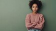 © Jittapon - Portrait of an anxious and thoughtful teenage African American girl wearing an oversized sweatshirt and ripped jeans standing against a plain olive green studio background with copy space above