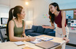 © Parichat - Two young businesswomen are having a cheerful discussion about work, reviewing financial charts and data on a laptop and paperwork