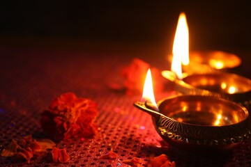 Wall Mural - Diwali celebration. Diya lamps and beautiful flowers on dark background, closeup. Space for text