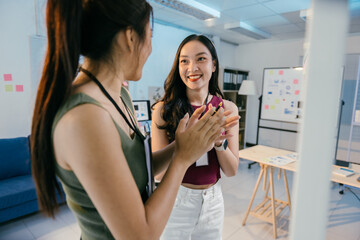 Two young businesswomen celebrate success in a modern office, clapping happily after a meeting. Bright space with desks, computers, and charts. Colleagues in casual attire, professional look