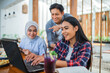 © Odua Images - a young woman types on a laptop during group work with friends at a cafe